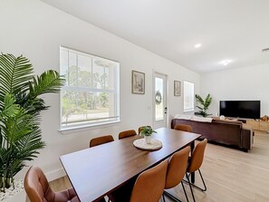 A modern living room with a dining area, large windows, a flat-screen TV, and a potted plant. - 15261 Brainbridge Circle, Port Charlotte, FL 33981 (Charlotte County)