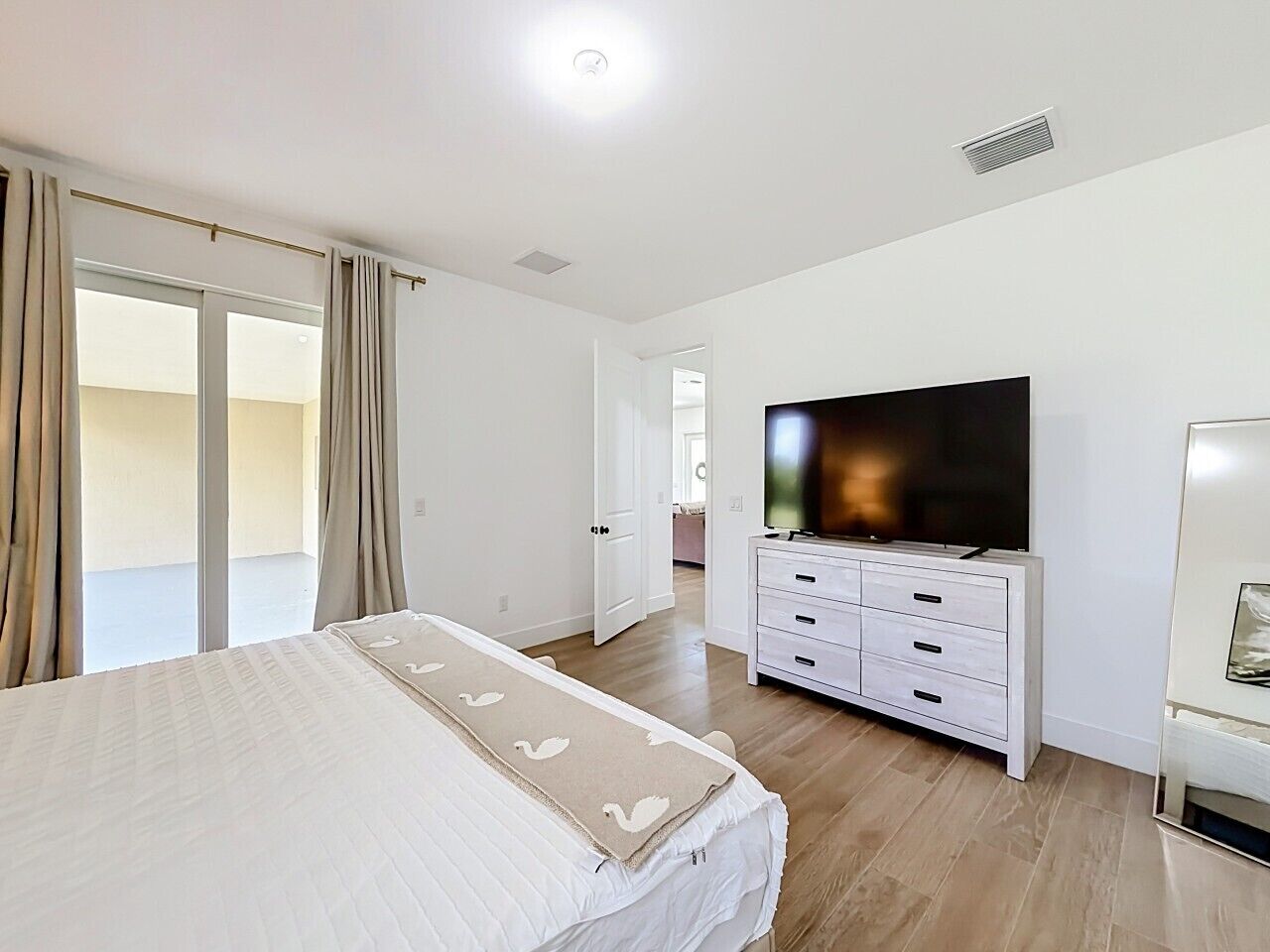 A bedroom with a bed, a TV, a dresser, and a sliding glass door leading to a balcony.