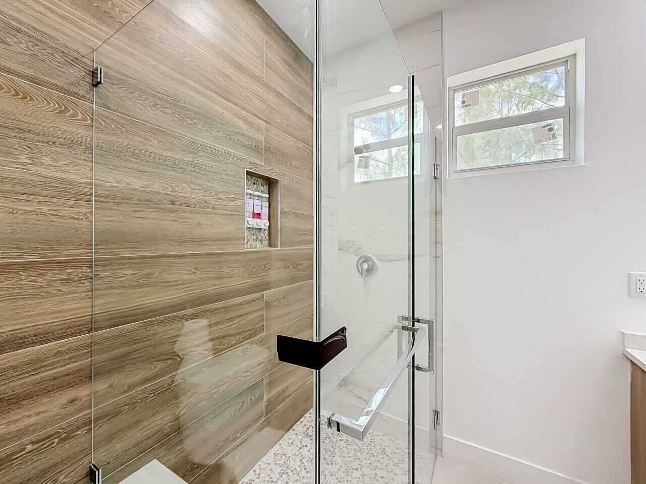 A modern bathroom with a glass shower enclosure, wooden wall panels, and a small window.
