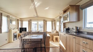 A caravan interior with a dining area, kitchen, and seating space. - 23 Gull Court (Porthmadog)