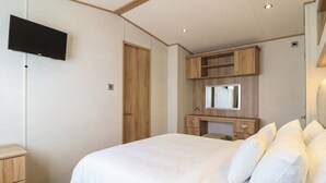 A bedroom with a bed, a television mounted on the wall, a wooden dresser, and a mirror above the dresser. - 23 Gull Court (Porthmadog)