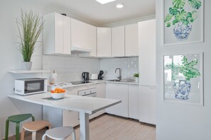 Een moderne keuken met witte kasten, een magnetron, een spoelbak en een potplant.
