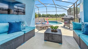 Un espacio al aire libre techado con mobiliario de mimbre, piscina y una parrilla.