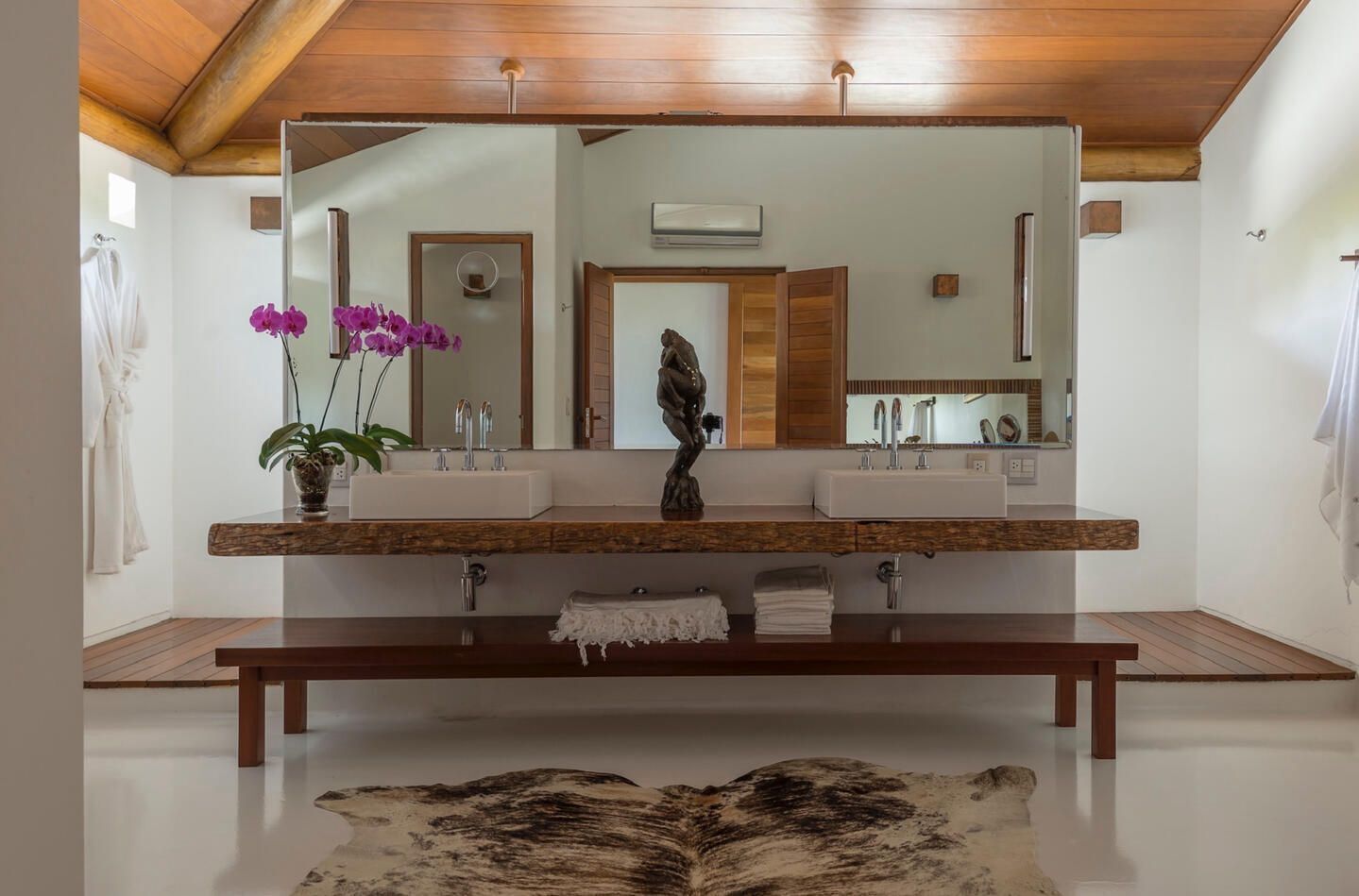 A modern bathroom with a large mirror, two sinks, a bench, and a potted plant. - House with sea and cliff views, 100m from the beach in Trancoso. (Trancoso)