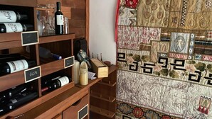 A wooden wine rack with bottles and glasses, a small figurine, and a patterned tapestry. - House with sea and cliff views, 100m from the beach in Trancoso. (Trancoso)