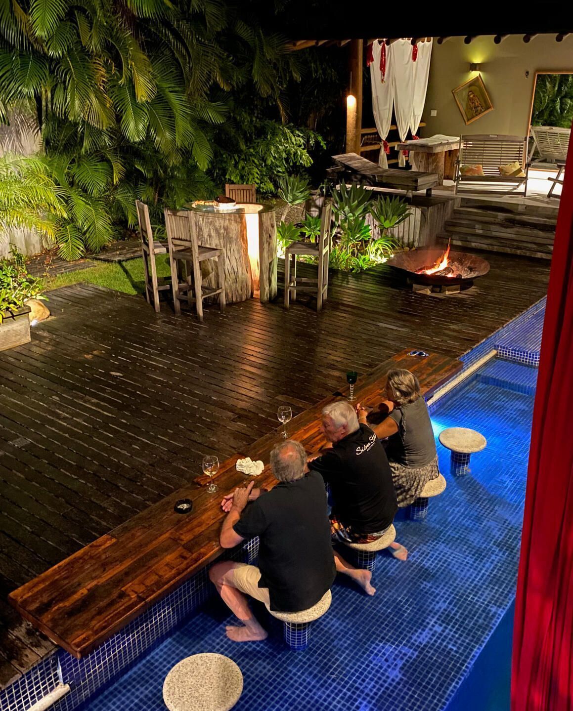A bar area with wooden furniture, a fire pit, and a pool with blue tiles.