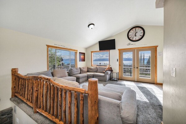 A spacious living area with a wooden staircase, a large window, and a clock on the wall.