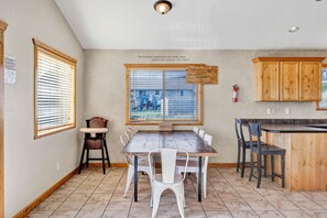 A dining area with a wooden table and chairs, a large window with blinds, and wooden cabinets.
