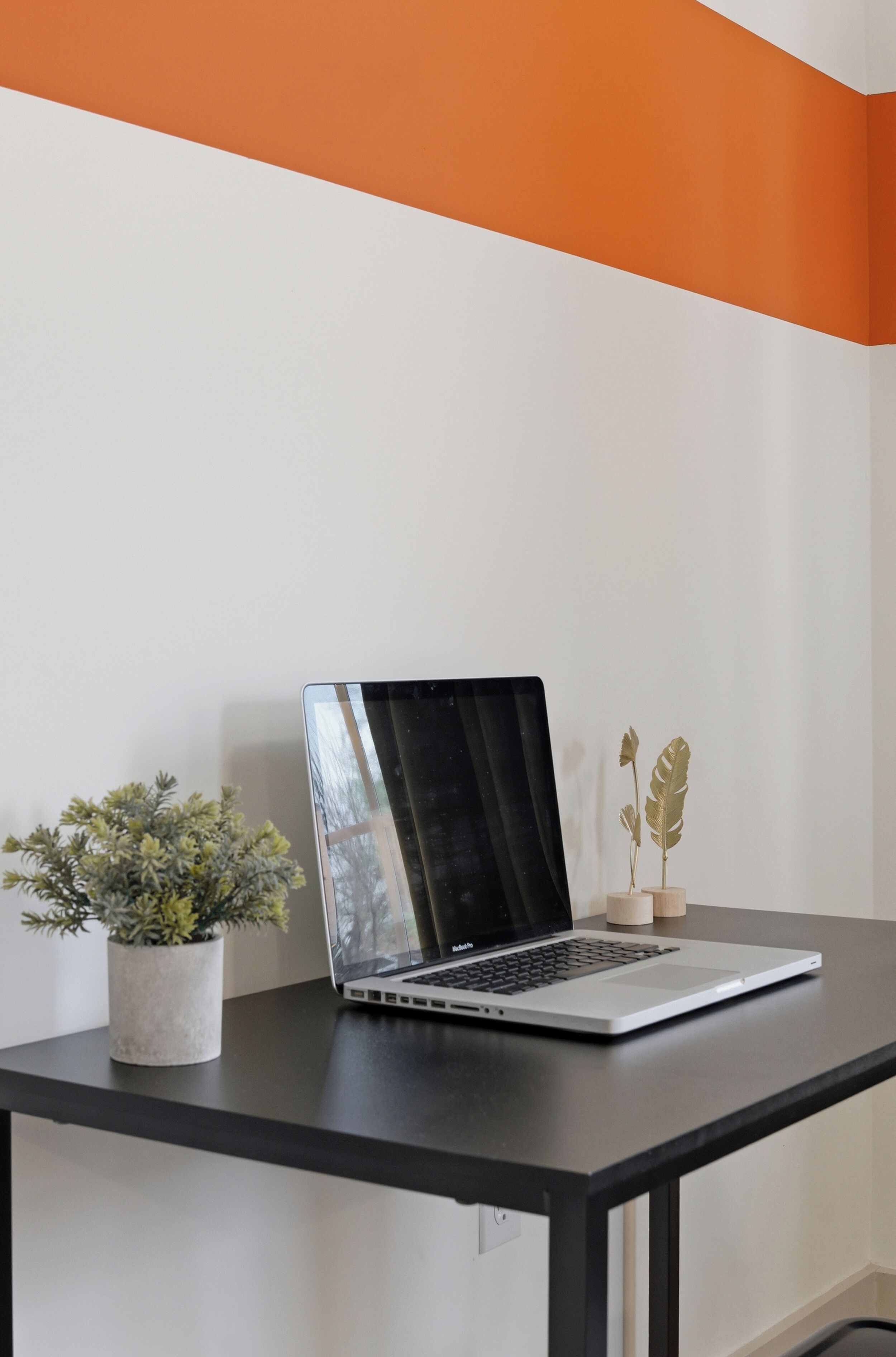 A laptop on a black table with a white and orange wall in the background.
