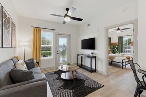 A modern living room with a sofa, a coffee table, a TV, and a ceiling fan. - The Lofts On Maney (Murfreesboro)