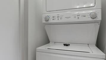 Eine weiße Waschmaschine und ein Trockner stehen übereinander in einer Ecke eines Raumes mit weißen Wänden.