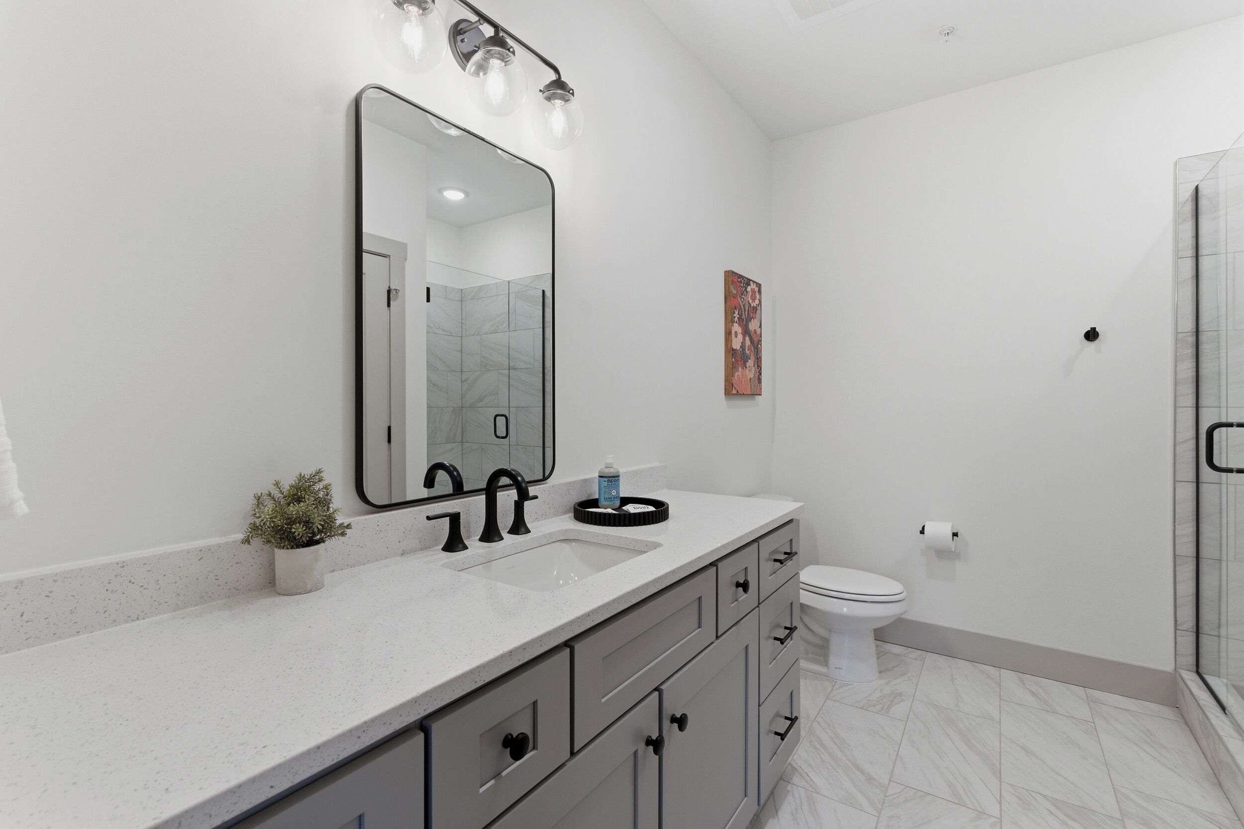 Une salle de bain moderne avec un grand miroir, deux lavabos, des toilettes et un espace douche.