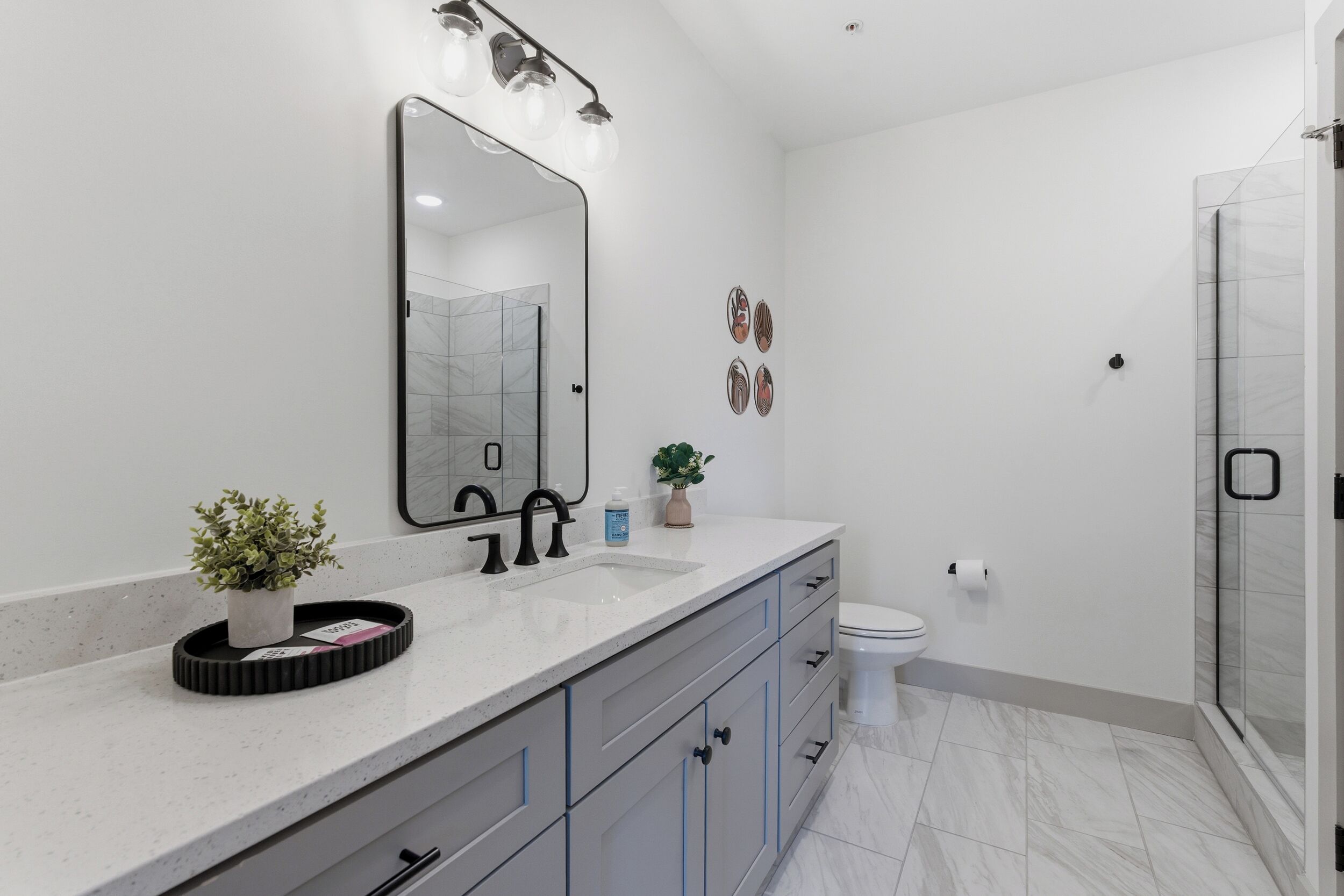 Un baño moderno con un espejo grande, un lavamanos, un inodoro y una zona de ducha.