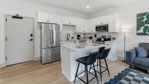 A modern kitchen with white cabinets, stainless steel appliances, and a central island with bar stools. - The Lofts On Maney (Murfreesboro)