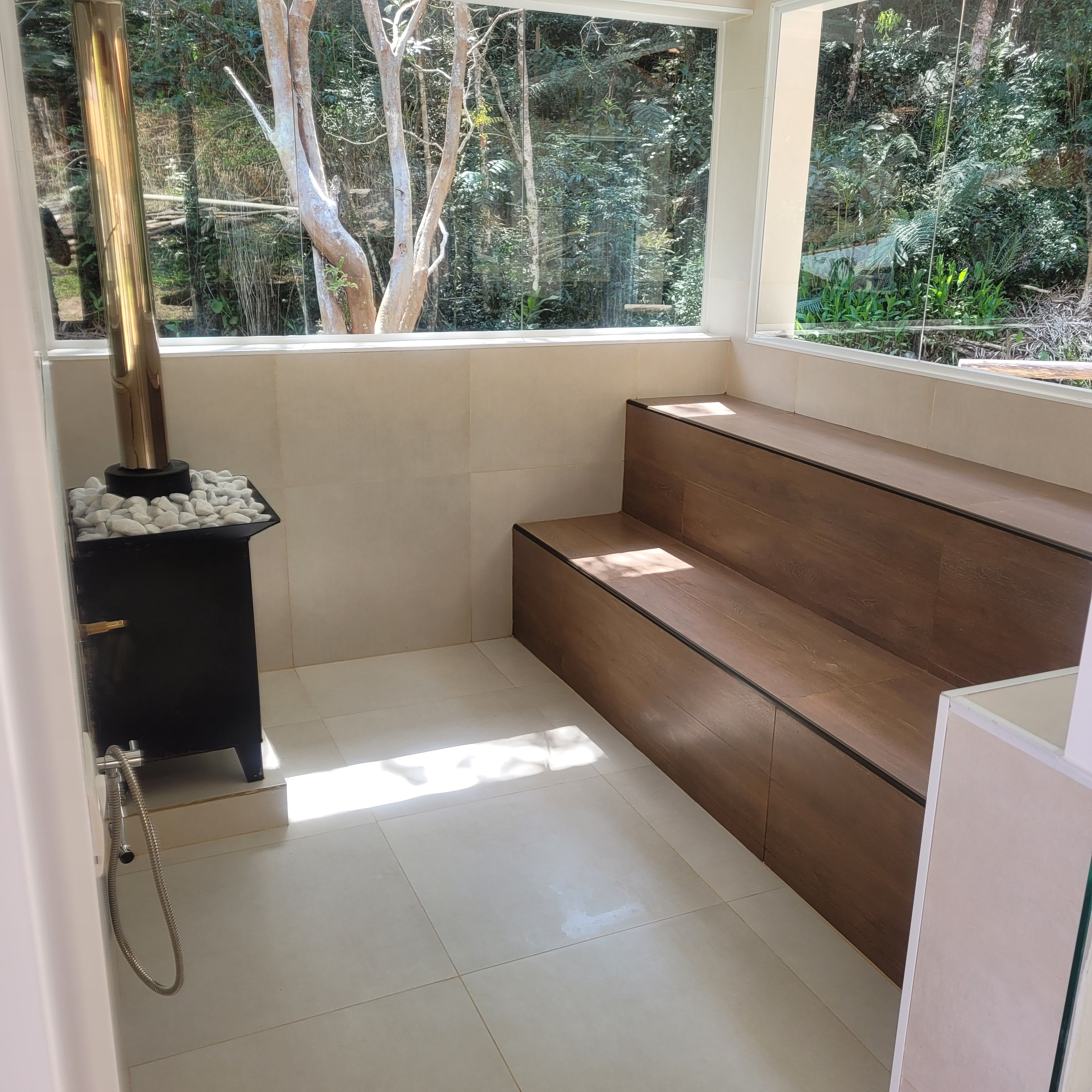 A modern bathroom with a built-in bench, a shower with a handheld hose, and a view of the outdoors through a large window.