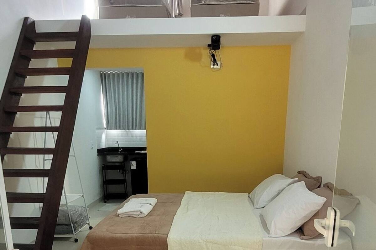 A bedroom with a bed, a wooden ladder, a window with curtains, and a yellow wall.