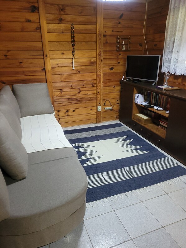 A cozy room with a wooden wall, a sofa, a TV on a stand, and a patterned rug. - Sitio Altezza (Salesópolis)