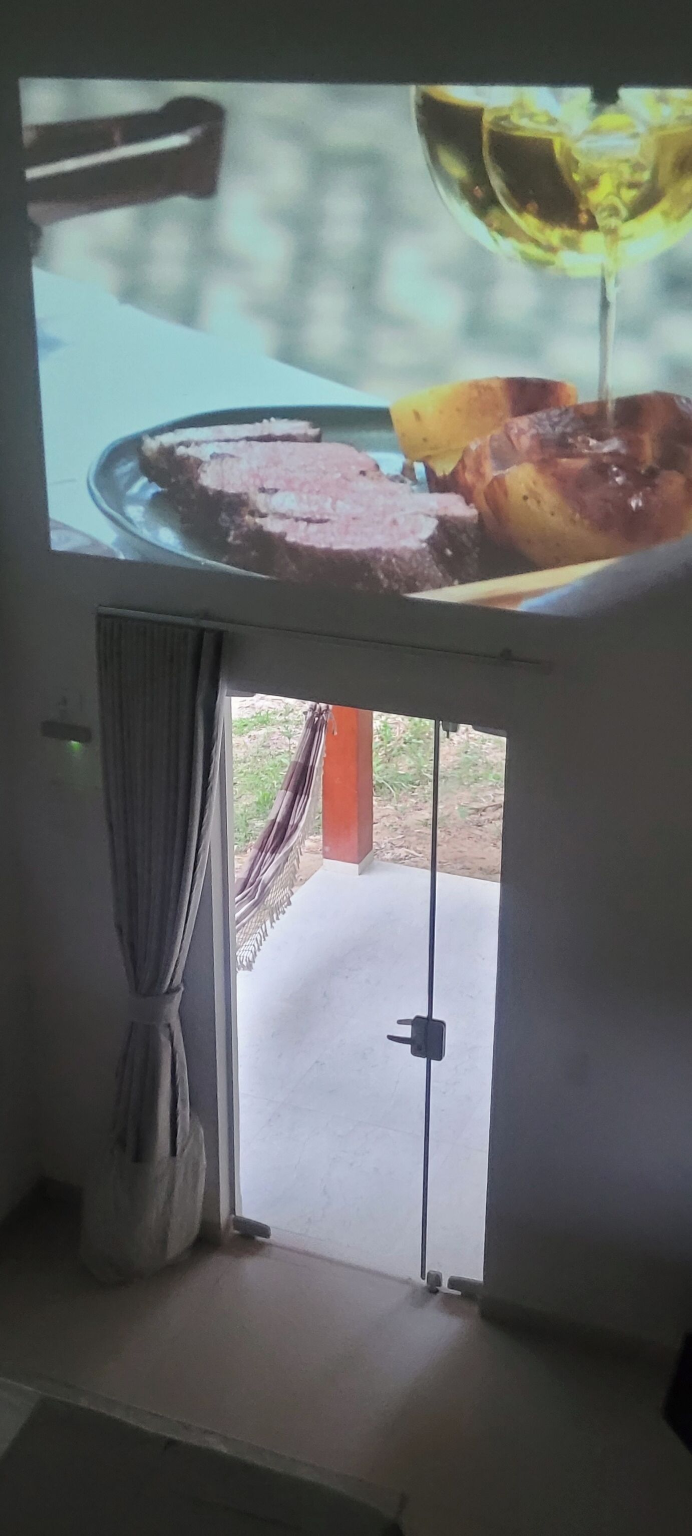 A room with a television displaying a meal, a door leading outside, and a curtain.