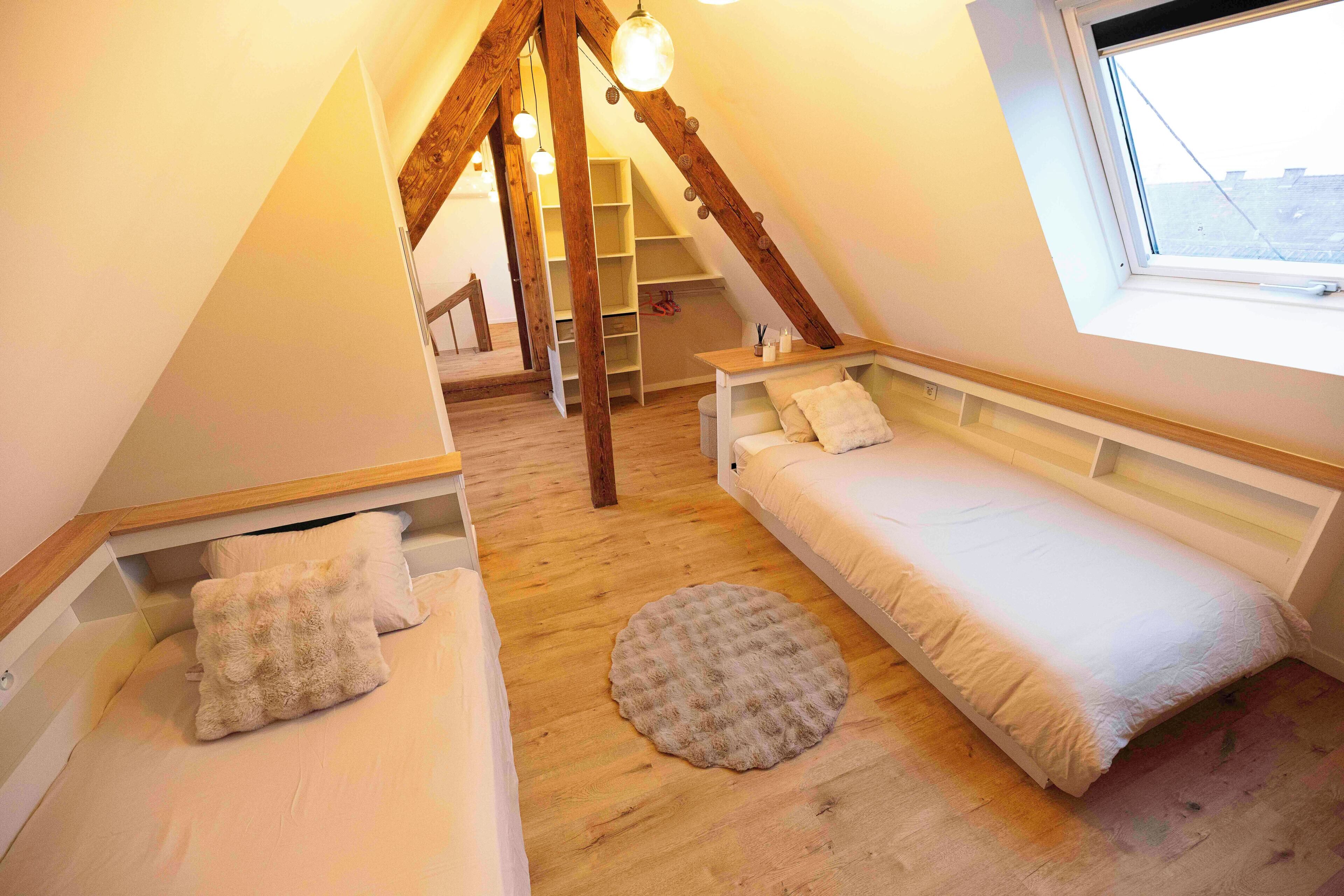 Una camera da letto mansardata accogliente con due letti, una scala in legno e un lucernario.