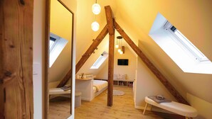 A loft bedroom with skylights, a wooden beam ceiling, a small bench, and a white bed.