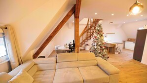 A modern living room with a large beige sectional sofa, a wooden staircase, and a decorated Christmas tree.