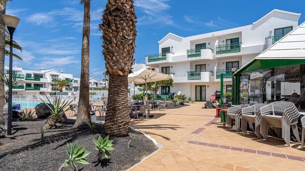 Ein Resort mit Außenbestuhlung, Palmen, einem Pool und einem weißen Gebäude mit Balkonen.