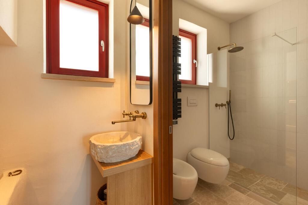 Une salle de bain avec un lavabo en pierre, des toilettes, une douche et un miroir.