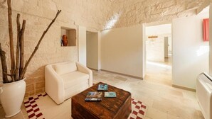 A room with a white sofa, a wooden coffee table with books, a potted plant, and a stone wall. - Trulli D Amore (Monopoli)