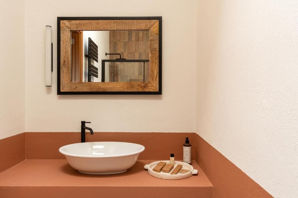 Un bagno con un lavandino bianco, uno specchio e articoli da toilette su uno scaffale.