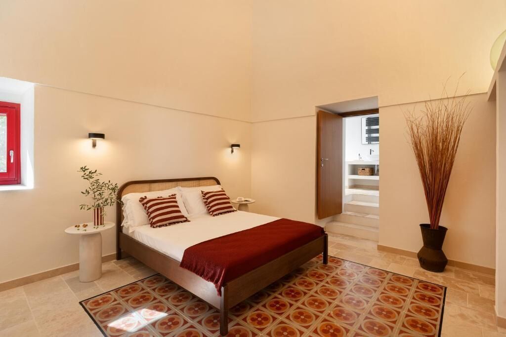 A bedroom with a bed, bedside tables, a potted plant, and a view of a staircase.
