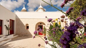 A building with white walls and red doors, a courtyard with gravel, and a clear blue sky. - Trulli D Amore (Monopoli)