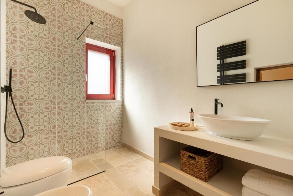 A bathroom with a toilet, shower, sink, and a mirror.