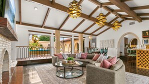 A spacious living area with a large sofa, a coffee table, and a fireplace. There are wooden beams on the ceiling and a view of the outside. - 20 beds,2 pkleball+bball, 5 acre estate gameroom (Bermuda Dunes)
