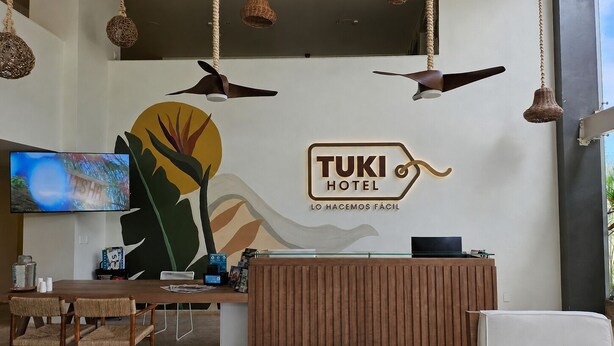 A reception desk with a TUKI HOTEL sign, a television, and a seating area with chairs and a sofa.