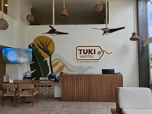 A reception desk with a TUKI HOTEL sign, a television, and a seating area with chairs and a sofa.