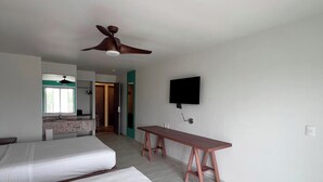 A room with two beds, a desk, a ceiling fan, a TV, and a bathroom visible in the background.