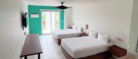 A modern hotel room with two beds, a desk, a small table, a round seating area, and a view of the outdoors.
