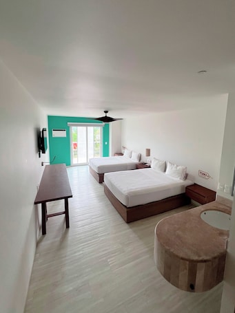 A modern hotel room with two beds, a desk, a small table, a round seating area, and a view of the outdoors.. Hotel Tuki Tulum