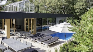A modern outdoor pool area with lounge chairs, a glass-enclosed structure, and a view of a swimming pool. - Unique 6 bed 5 bath cottage on Lake Muskoka with Pool (Gravenhurst)
