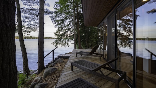 A wooden deck with a bench and a table, overlooking a calm lake with trees. - Unique 6 bed 5 bath cottage on Lake Muskoka with Pool (Gravenhurst)