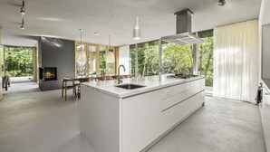 A modern kitchen with a large island, white cabinetry, and a view of greenery outside. - Unique 6 bed 5 bath cottage on Lake Muskoka with Pool (Gravenhurst)