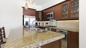 Eine Küche mit Granit-Arbeitsplatten, Edelstahlgeräten, Holzschränken und Pendelleuchten.