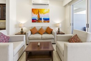 A modern living room with a sofa set, a coffee table, and a painting of a sailboat on the wall. - One Bedroom Oceanfront - Puerto Escondido 1352 (Bajos de Chila)