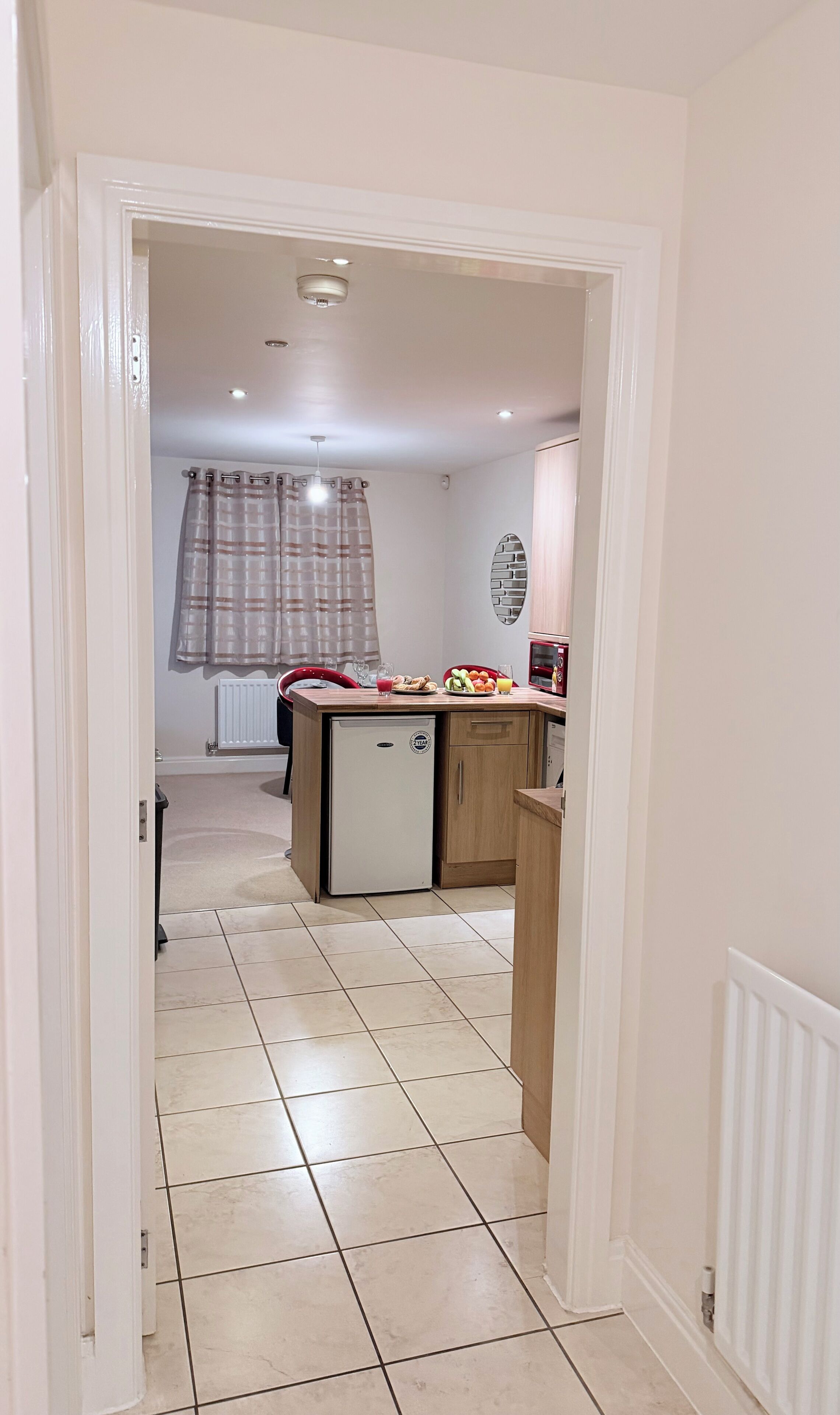 A narrow hallway leading to a kitchen with a refrigerator, a microwave, and a small island with food items.