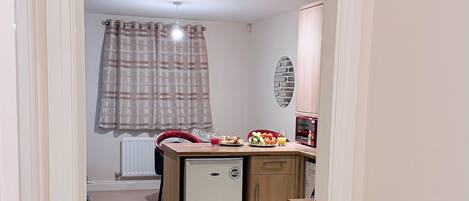 A narrow hallway leading to a kitchen with a refrigerator, a microwave, and a small island with food items.