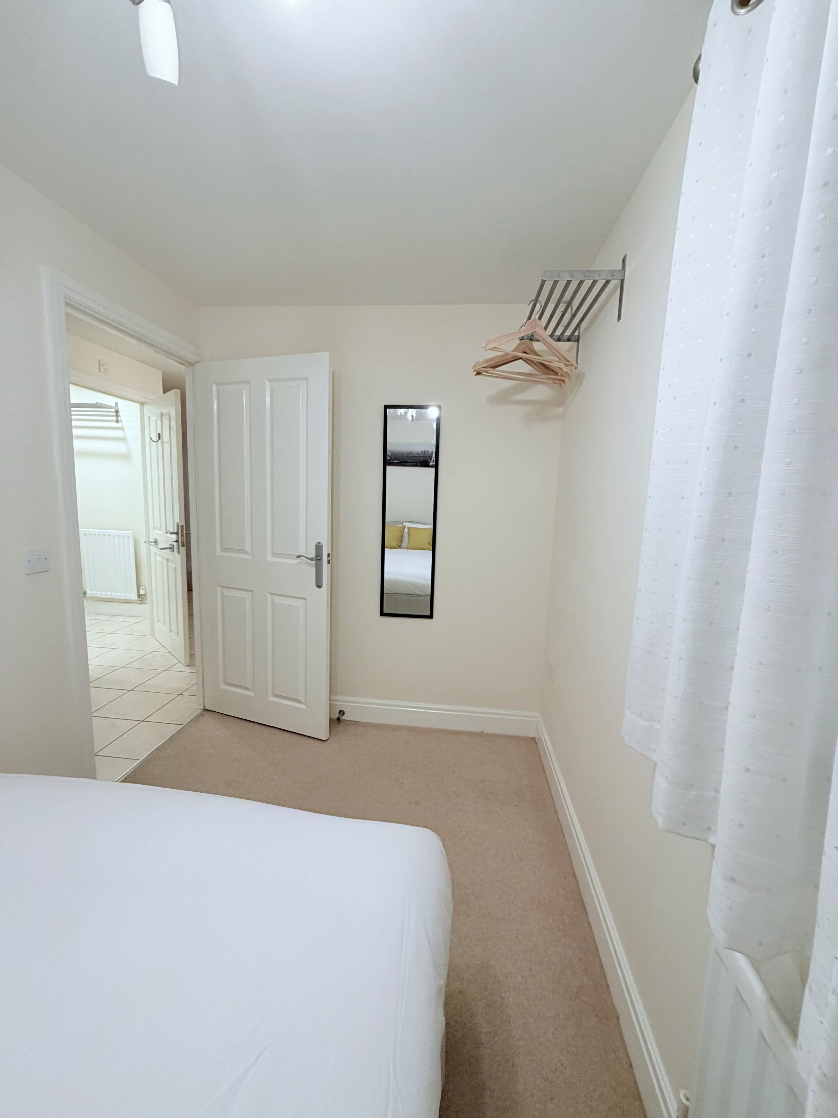 A bedroom with a bed, a door, a mirror, and a hanging rack.
