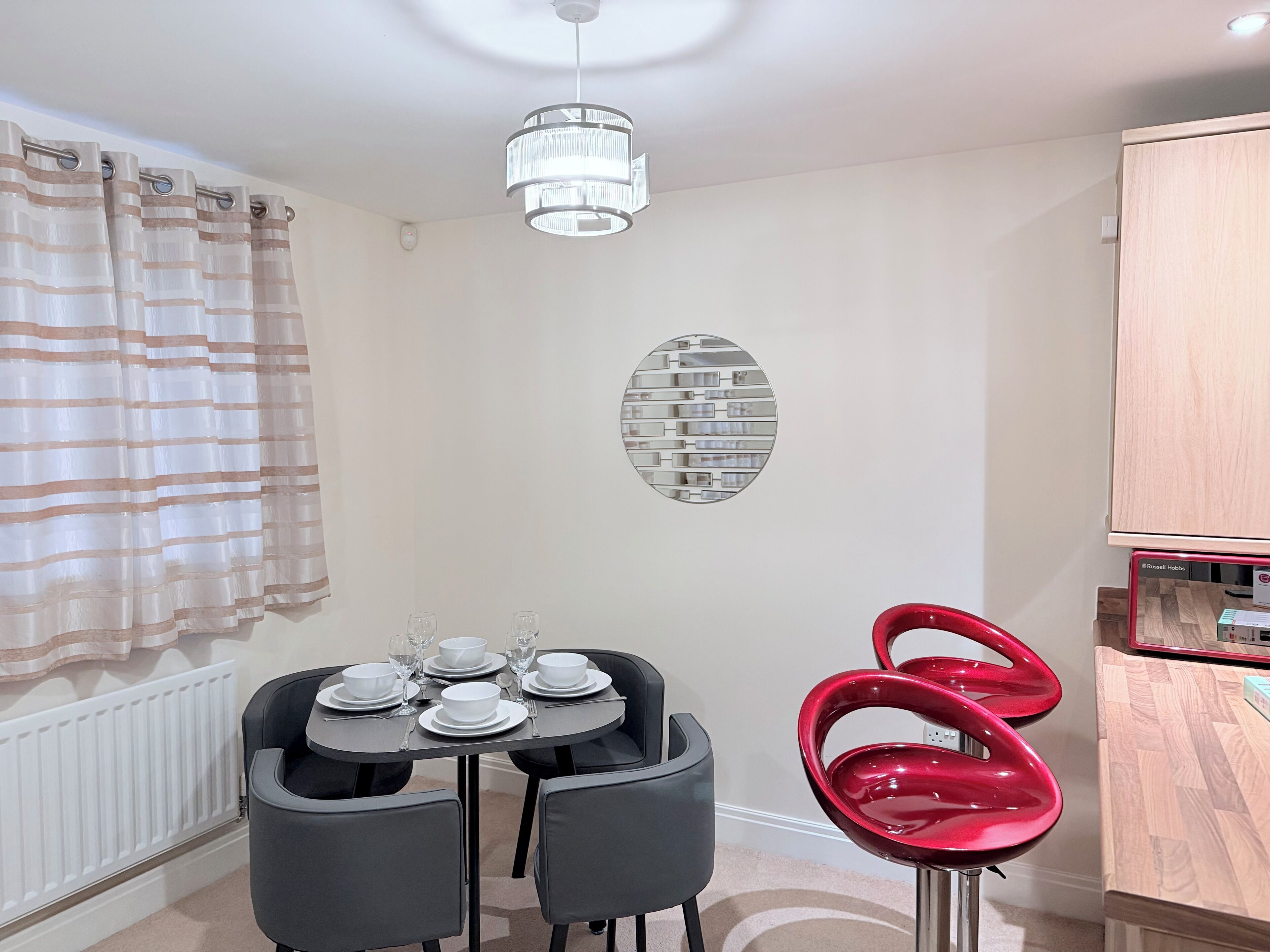 Ein Essbereich mit einem Tisch für vier Personen, zwei schwarzen Stühlen, einem roten Stuhl, einer Kronleuchter und einer an der Wand befestigten Regal mit Ziegeloptik.