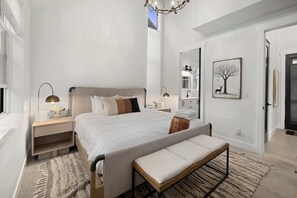 Una camera da letto moderna con un letto grande, comodini, una panca, un lampadario, uno specchio e un quadro appeso al muro.