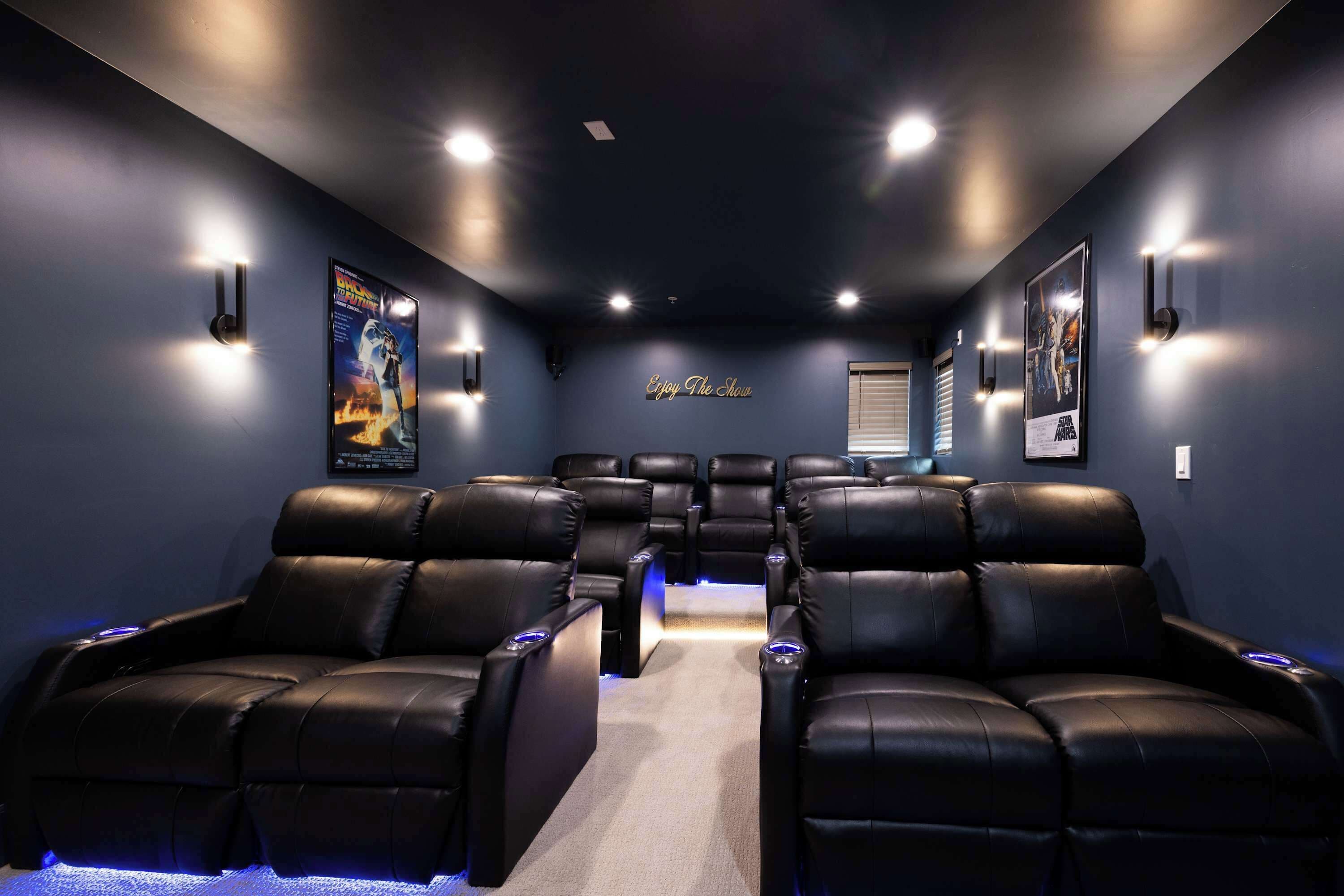 Une salle de cinéma privée avec des fauteuils inclinables en cuir noir, un sol recouvert de moquette et un éclairage fixé au mur.