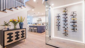 A modern kitchen with a central island, a glass-fronted wine display, and a staircase leading to an upper level. - HÓZHÓ | Private Pool, Hot Tub, Bowling & Fire Pit (Scottsdale)